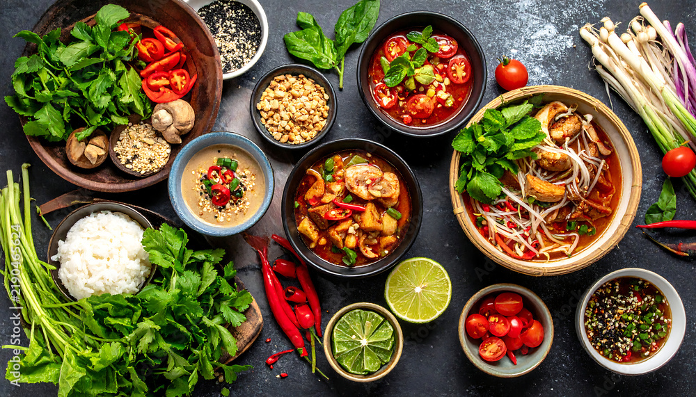 © Maski - Flat lay of healthy Vietnamese cuisine featuring traditional bowls of soup, fresh herbs, steamed rice, and spicy condiments on a dark background