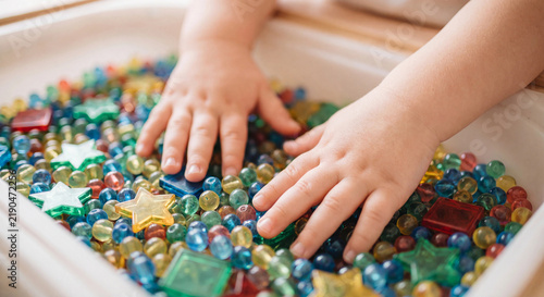 Child hands playing with colorful beads in sensory tray photo for early learning
