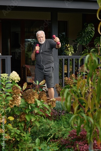 Man exercising with dumbbells in a garden during the afternoon