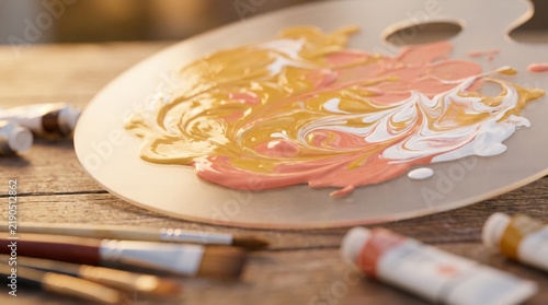 Artist palette with mixed paint and brushes on wooden desk