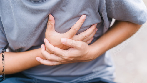 Quadro su tela Close-up of an adult man tightly grabbing his chest outdoors, suffering from severe chest pain, heart attack, or cardiovascular problem