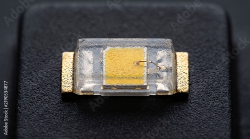 Surface mount led with transparent housing and yellow phosphor on dark textured background.