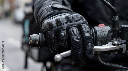 Macro shot of rider gloved hand gripping rainy wet motorcycle handlebar and brake lever