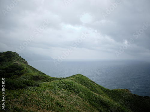 Fotografie Green grassy hills sloping down to the sea under a gray sky Hokkaido