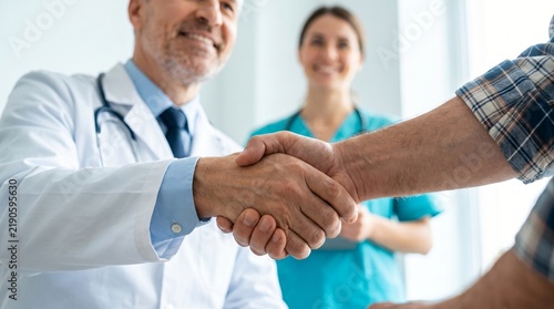 close-up Doctor handshake hand with patient, showing trust and care. Nurse smiling , standing behind, offering support. Bright, clean room suggests professional medical setting. Image conveys positive