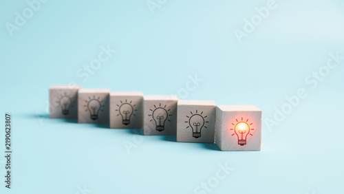 Canvas Print Row of wooden cubes with light bulb icons and one glowing bulb in front symbolizes standout ideas, innovation, leadership, creativity, inspiration, differentiation, and business success