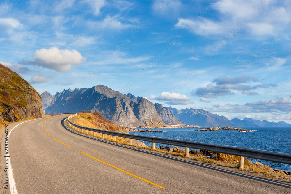 Obraz premium An empty asphalt road winding along a rocky sea coast with mountains under a blue sky