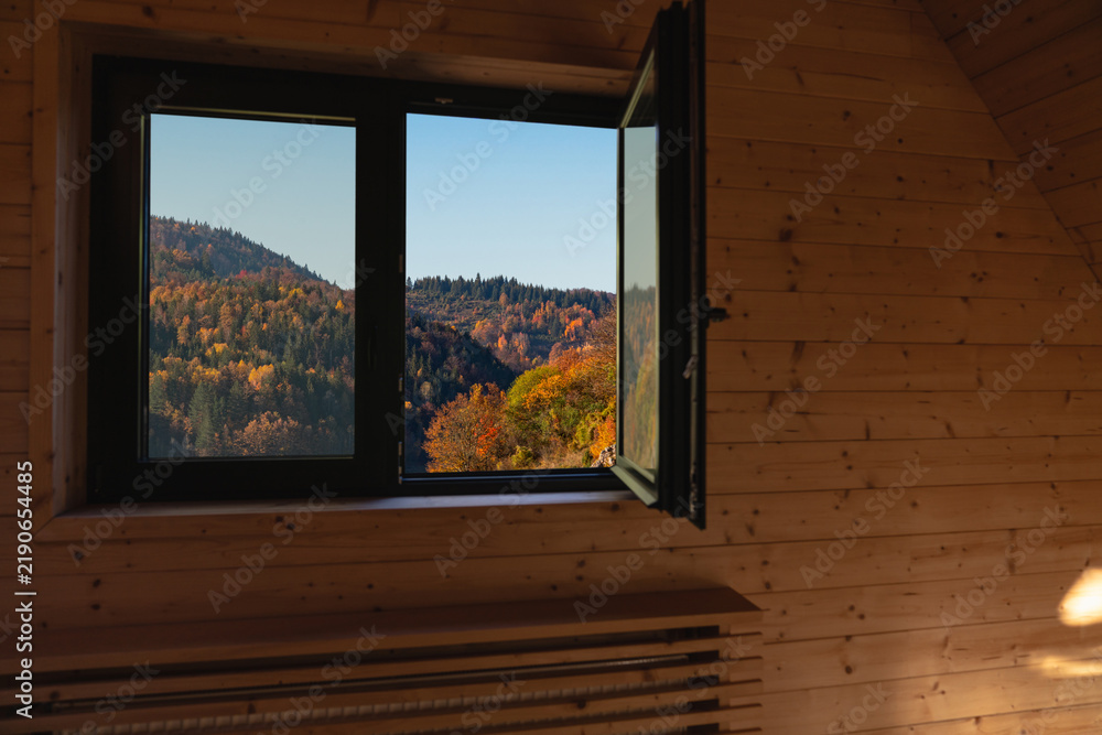 Obraz premium An open window in a wooden cabin looking out at colorful autumn forest