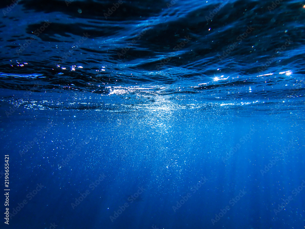 Obraz premium Underwater background with water bubbles and undersea light rays shine. Dark blue ocean surface seen from underwater. Sunbeams and Sea deep or ocean underwater a Abstract background. sunlight Nature.
