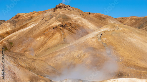 Foto A wooden boardwalk climbs golden mineral-stained hills toward billowing geothermal steam near Kerlingarfjoll, Icelandic highlands