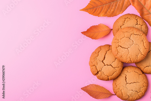 Homemade round cookies and autumn leaves arranged along the right side of a bright pink background with copy space.