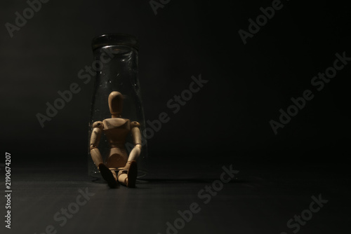 Картината върху платно Wooden mannequin trapped sitting inside a glass jar on dark black background, concept of isolation, quarantine, depression, confinement, or feeling stuck