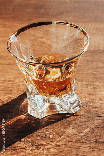 Фотография Clear glass with whisky resting on wooden surface in afternoon light
