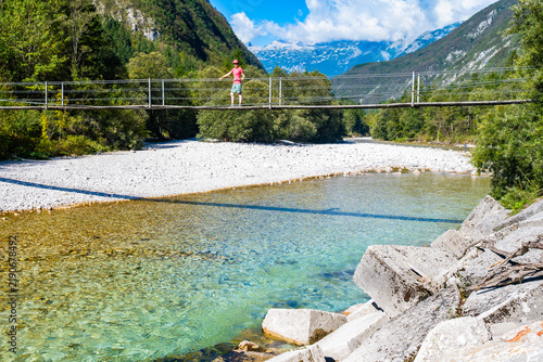 Obraz na płótnie Hiker standing on a wooden footbridge spanning the emerald Soca River with tower