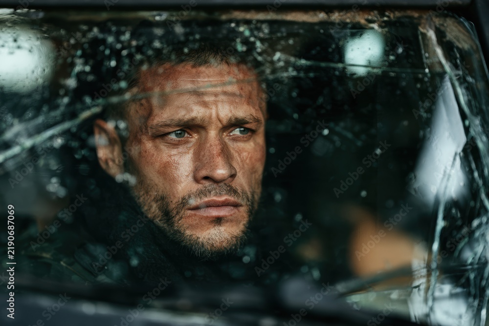 Obraz premium Scarred soldier man looking through a shattered windshield from inside a vehicle