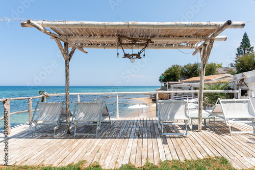 Patio with white umbrellas and sun loungers by the beach and sea in southern Italy on a summer day.