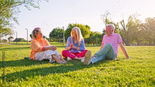 Group of stylish seniors sitting on grass, talking and enjoying sunny day