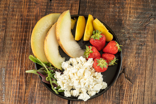Top view of a plate with fresh cottage cheese topped with sliced bananas, peach, and strawberries. Healthy organic breakfast, fruit and curd bowl.