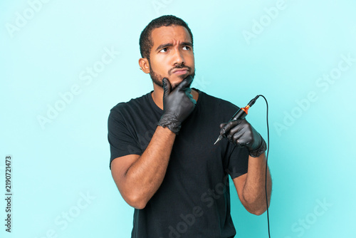 Obraz na plátně Tattoo artist Ecuadorian man isolated on blue background having doubts