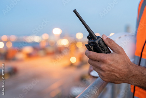 Worker holding a radio communicator at a busy shipping port  