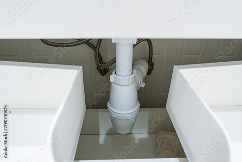 Bild auf Leinwand White bathroom sink cabinet plumbing with visible P-trap drain trap and braided