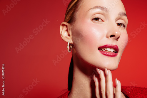 фотографія Close-up of a confident woman with red lipstick and hoop earrings posing against a red background