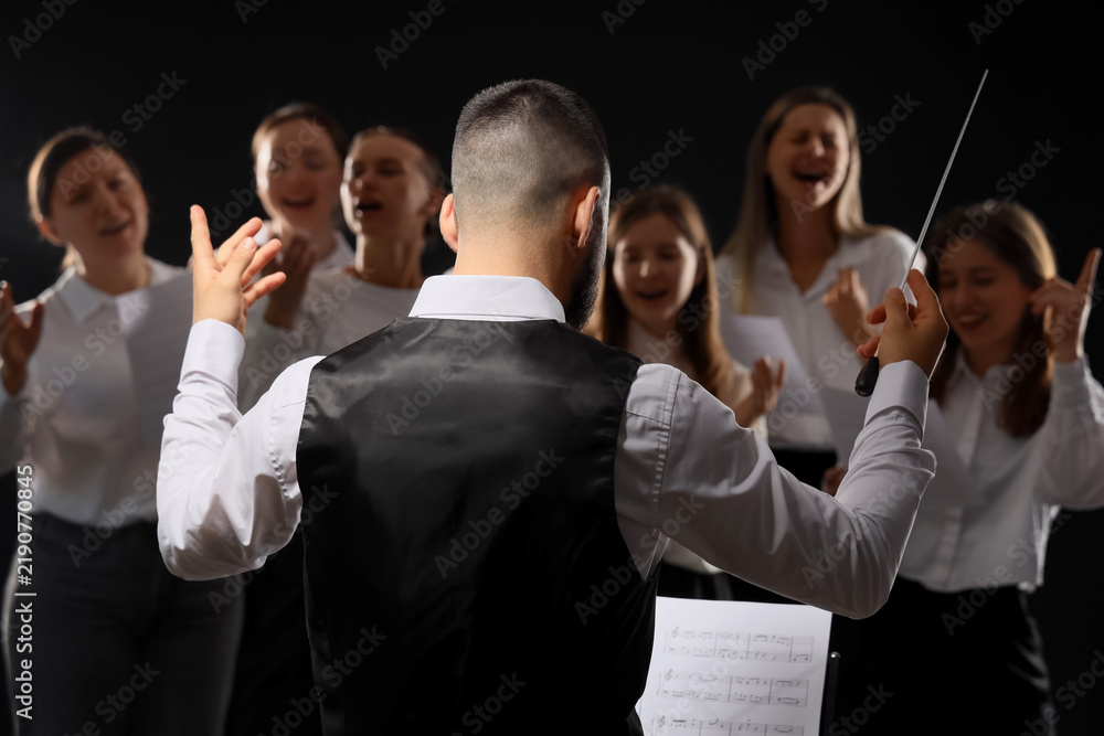 Obraz premium Leadership and teamwork, music conductor leading a choir with passion and precision during a performance on a dark stage with professional lighting