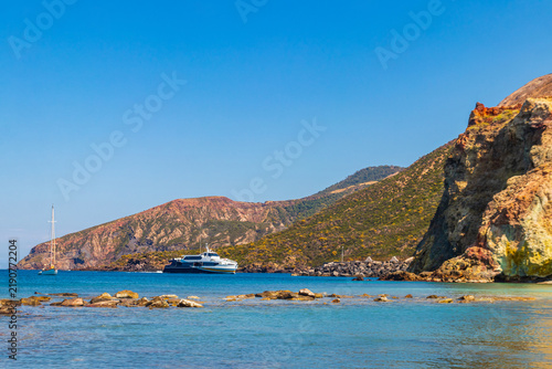 High-speed passenger ferry sailing in the blue Tyrrhenian sea past volcanic cliffs of Vulcano island, Aeolian archipelago, Sicily, Italy
