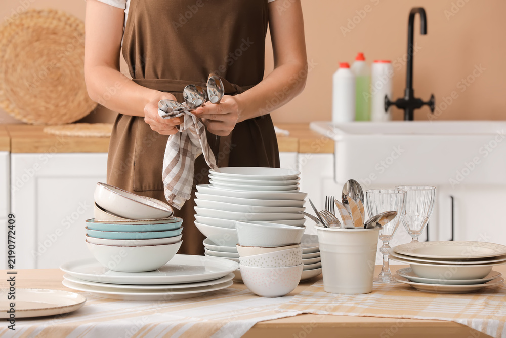 Obraz premium Household chores and kitchen hygiene, woman wiping clean cutlery with a towel after washing dishes in a home kitchen environment