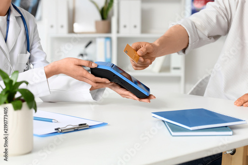 Male patient with credit card and doctor paying via terminal in clinic