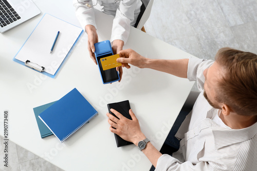 Male patient with credit card and doctor paying via terminal in clinic, top view