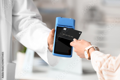Female hand with credit card and doctor paying via terminal in clinic, closeup