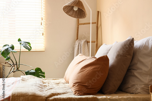 Cozy bed with soft pillows near beige wall in bedroom