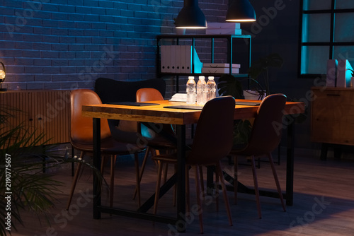 Interior of dark office with table, shelf unit and glowing lamps at night