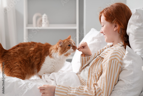 Redhead teenage girl with cute cat lying in bedroom