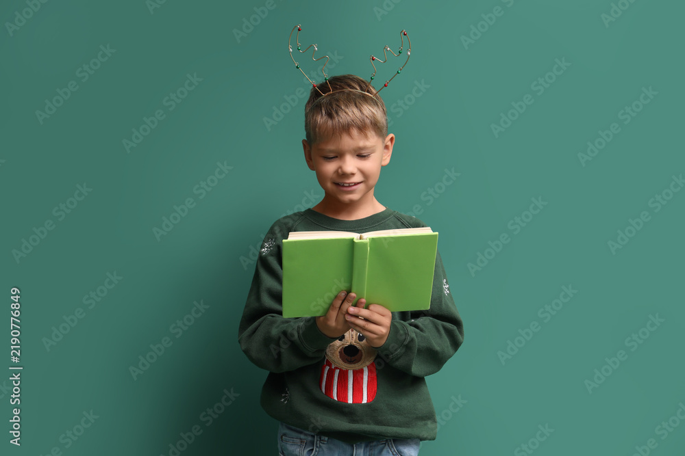 Obraz premium Cute little boy in reindeer horns reading Christmas story on green background