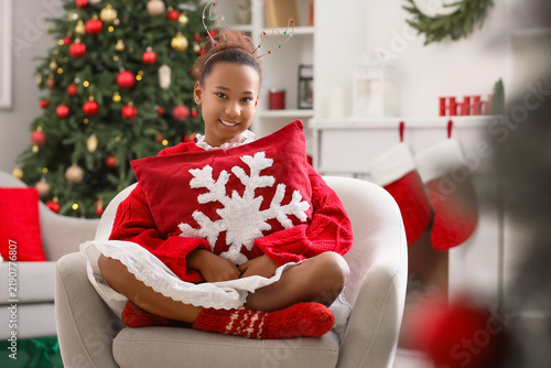 Teenage African-American girl with pillow sitting in armchair at home on Chri...