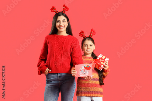Happy mother and her daughter holding Christmas gift with greeting card on re...