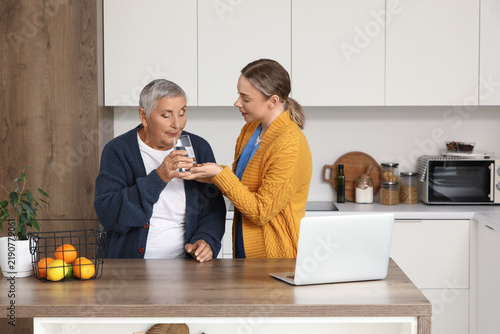 Senior woman drinking water with caregiver in kitchen