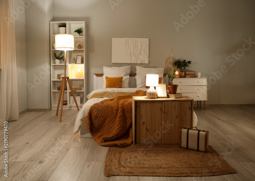 Interior of stylish bedroom with bed, shelving units, commodes and glowing la...