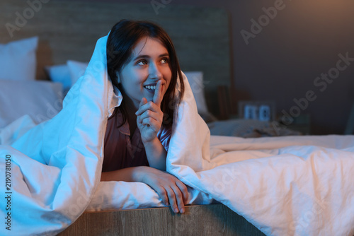 Young pretty woman under blanket resting on bed in bedroom at night