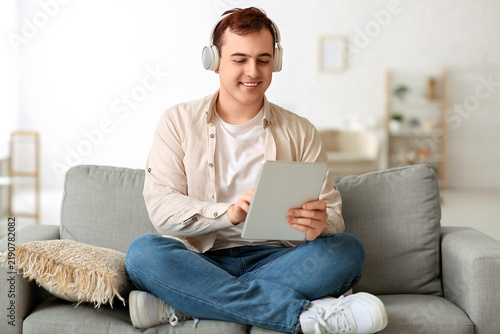 Young man listening to audiobook and using tablet in living room
