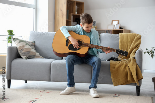 Teenage boy playing guitar on sofa in living room