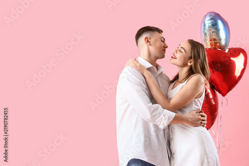 Happy young couple with beautiful heart-shaped balloons on pink background. V...
