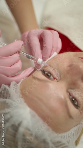 Cosmetologist makes facial injections near the eyes with a syringe. Concept of a procedure in a beauty clinic.