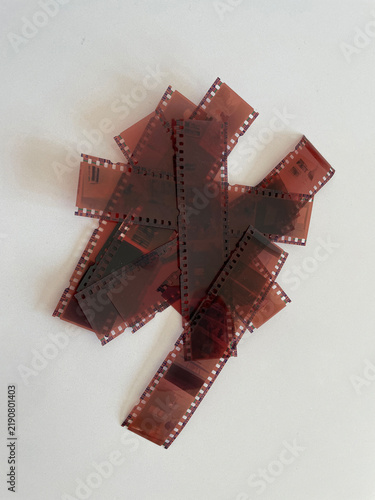Several strips of photographic negative film are piled together on a clean white surface. The classic film pieces are dark brown.