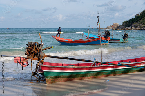 Traditional Thai longtail fishing boats and fisherman on sandy shore