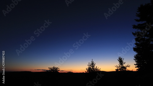 Tranquil twilight landscape in Quebec, Canada, with a deep blue sky fading into a warm orange horizon over tree silhouettes.