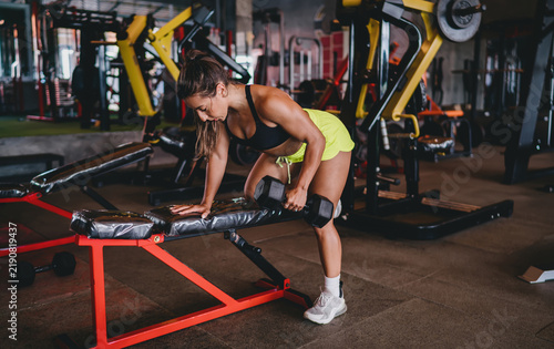 Obraz na plátně Side view of Hispanic athletic female performing stationary lunge with heavy dumbbells, strong woman training lower body muscles in gym, fitness determination, copy space