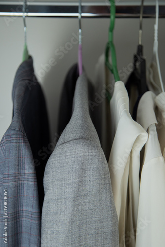 Canvastavla A close-up shows the upper part of a grey melange jacket and adjacent white clothes hanging on a steel rod with multicolored hooks